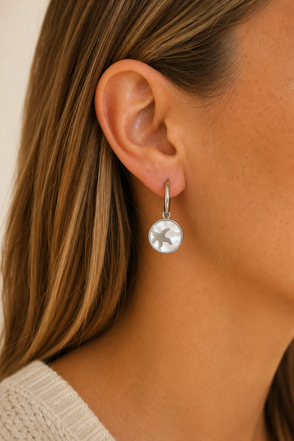Zilveren zeester parelmoer oorbellen in het oor van een vrouw, waterproof stainless steel damessieraad